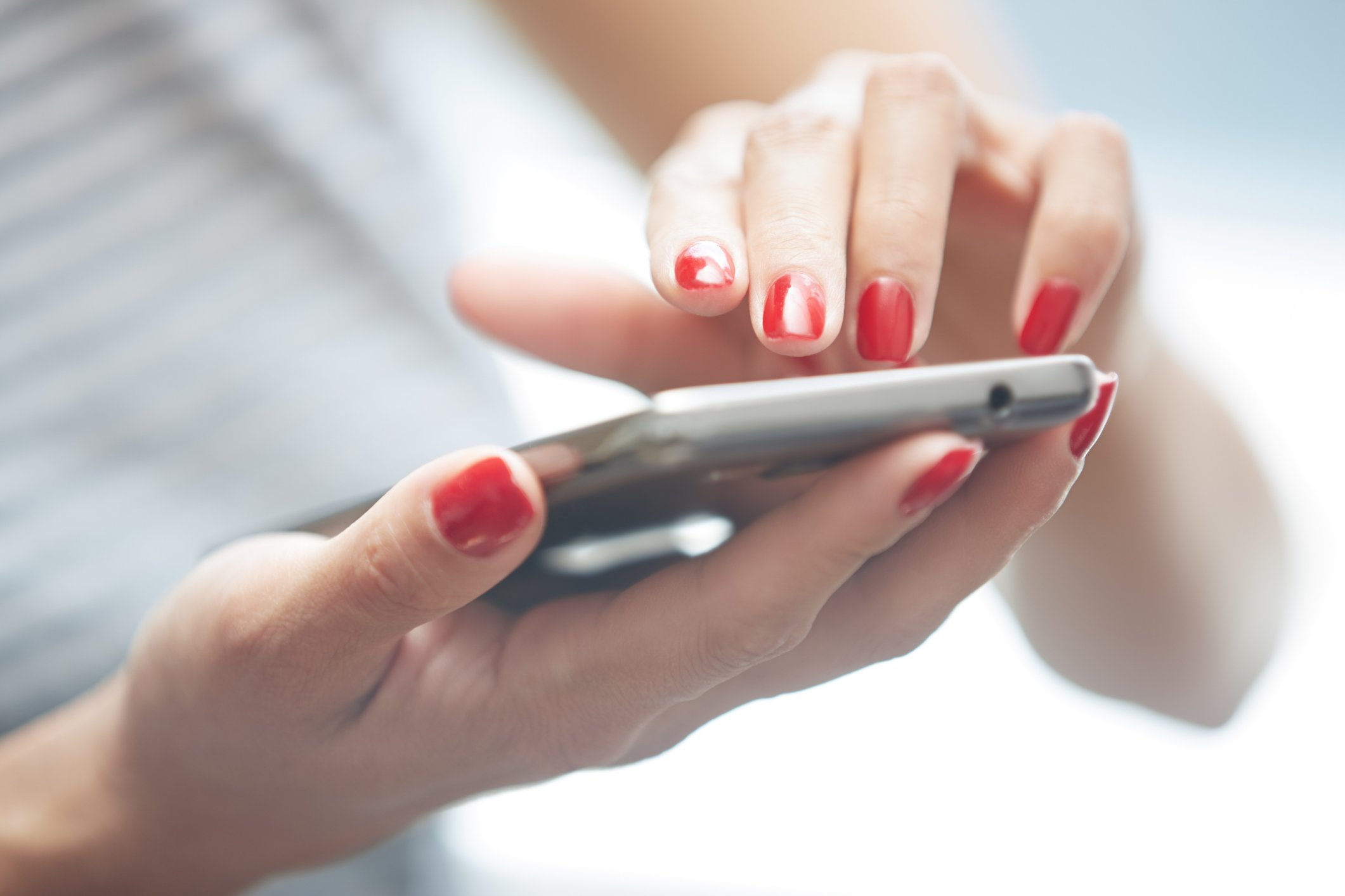 A woman's manicured hands typing on a mobile phone.