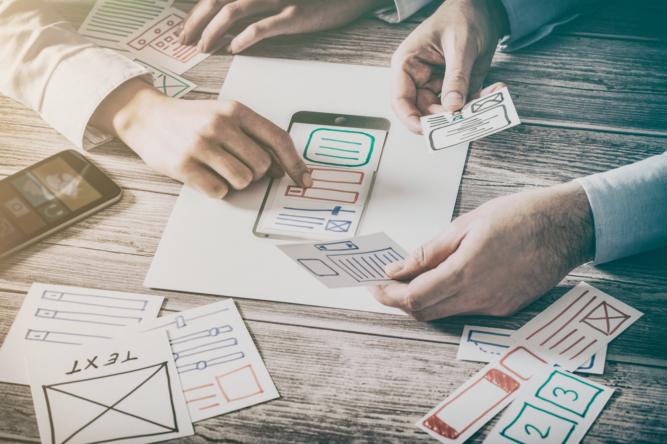 Two pairs of hands organizing website design on paper.