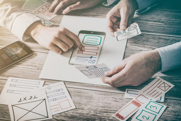 Two pairs of hands organizing website design on paper.