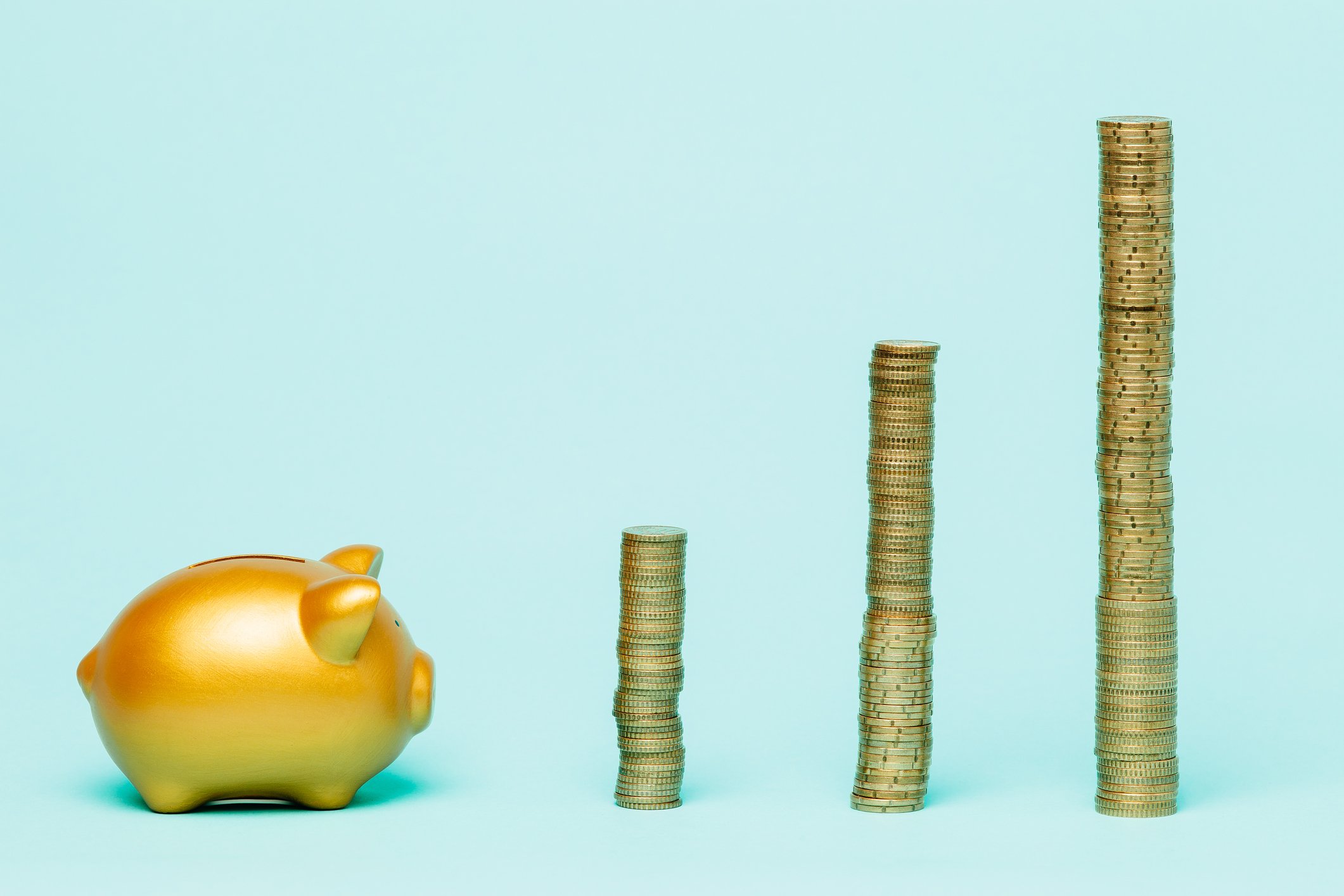 A golden piggy bank next to three stacks of gold coins.