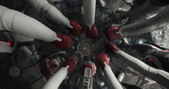 The Avengers put their hands in a circle, while Rocket Raccoon reaches up to join them, in a scene from Avengers: Endgame. 