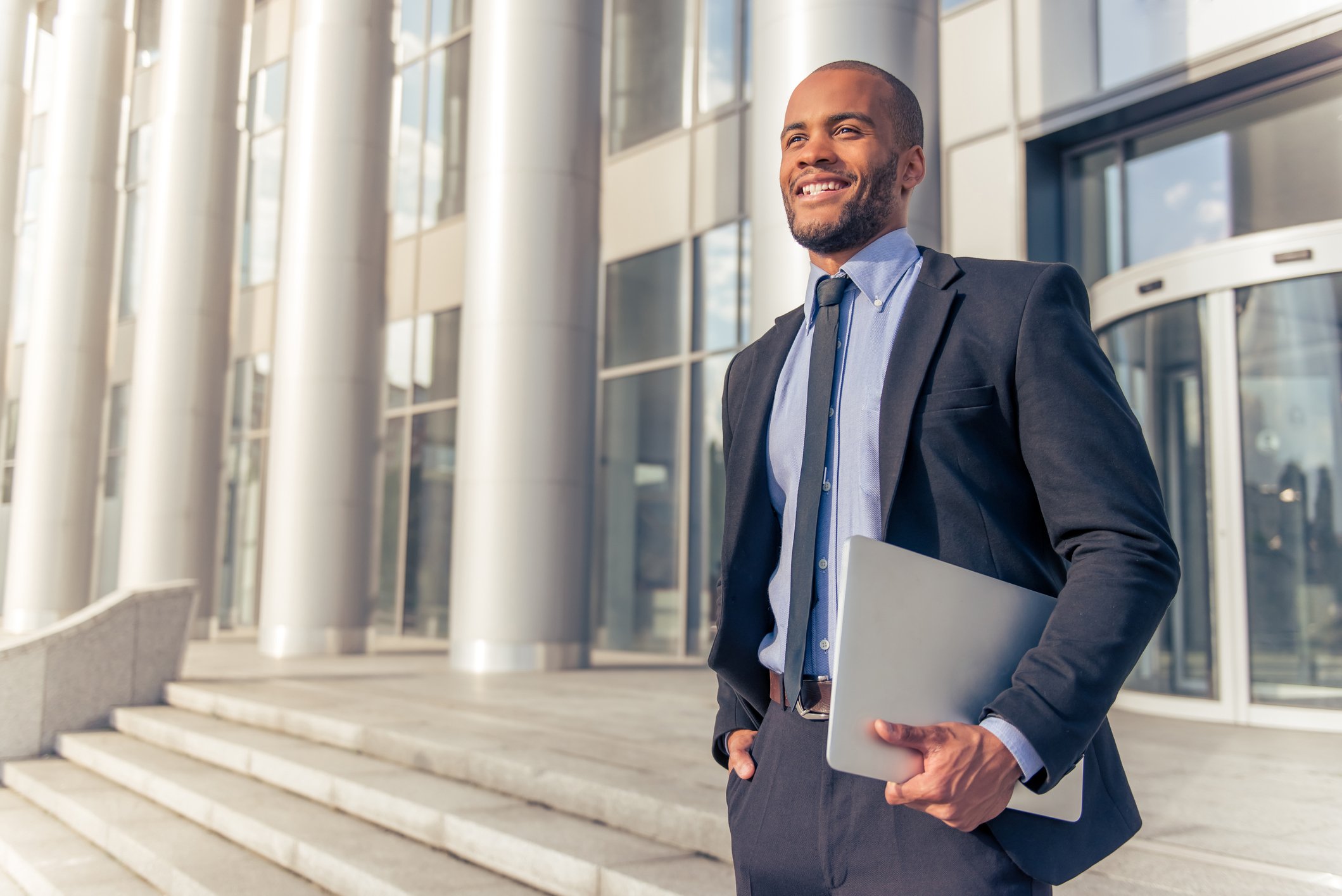Man holding laptop, standing on stairs in front of building