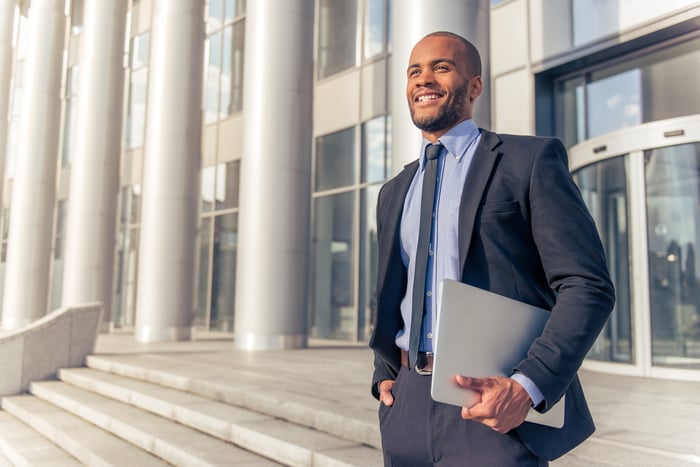 Man holding laptop, standing on stairs in front of building