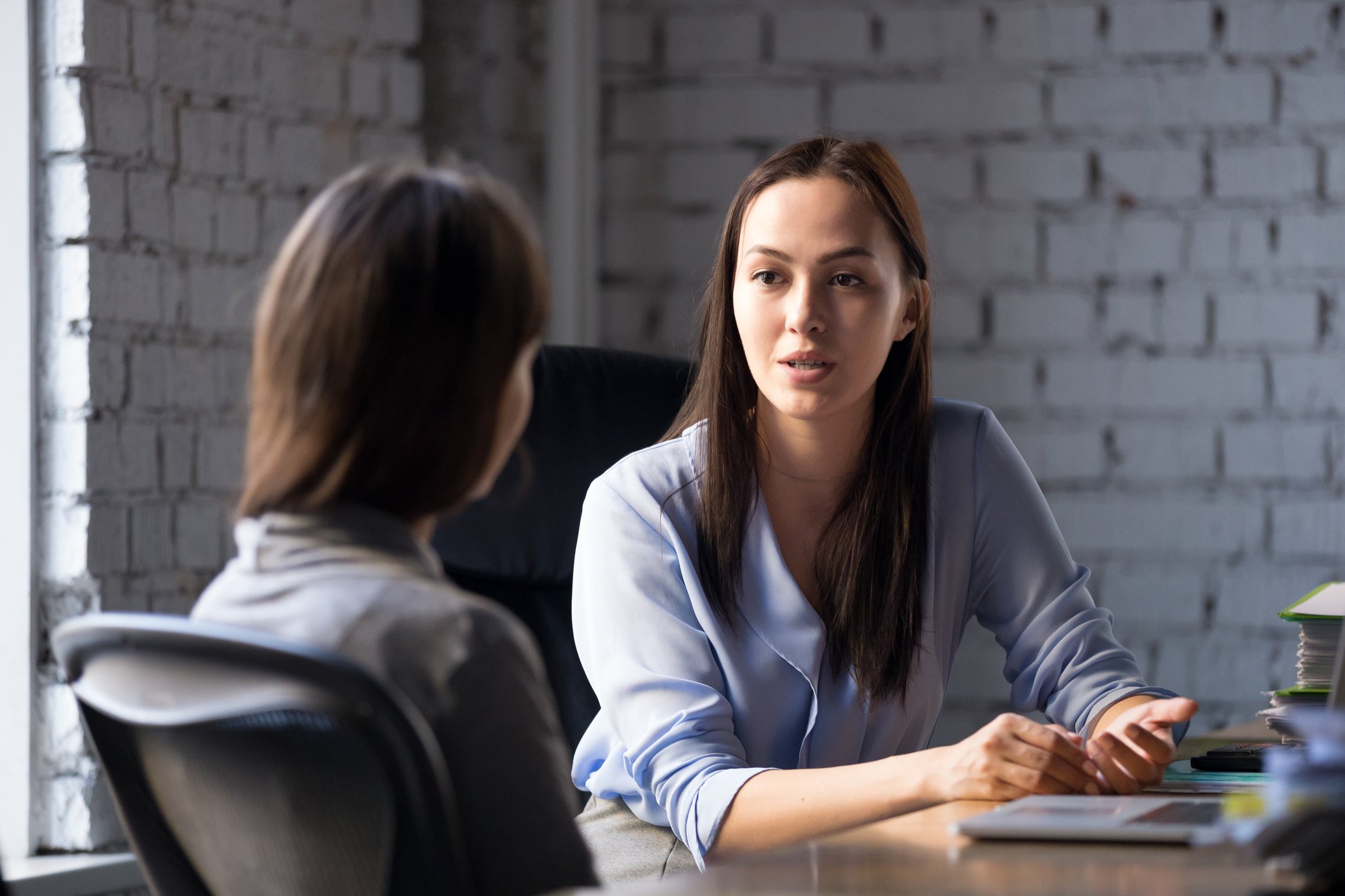 Professionally dressed woman with serious expression talking to another woman.
