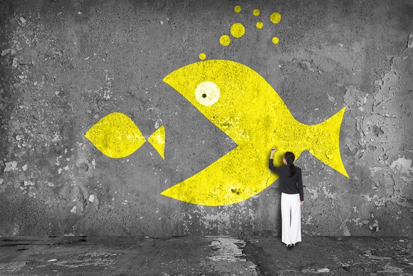 Woman drawing large yellow fish eating a smaller fish on a wall