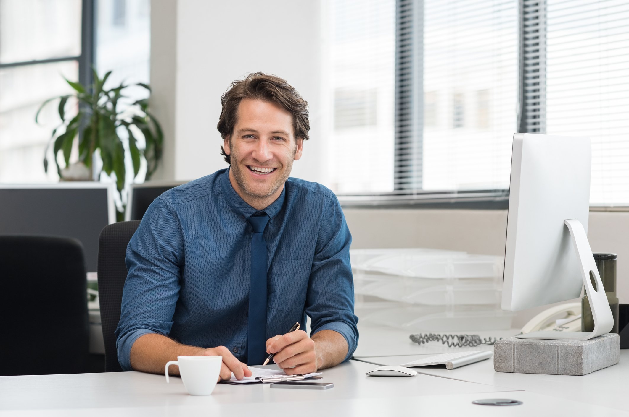 Smiling man sitting at desk, holding a pen