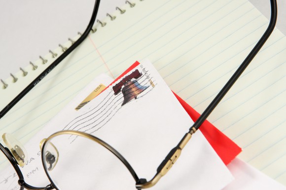 Envelope with forever stamp sitting on top of a notebook with glasses nearby