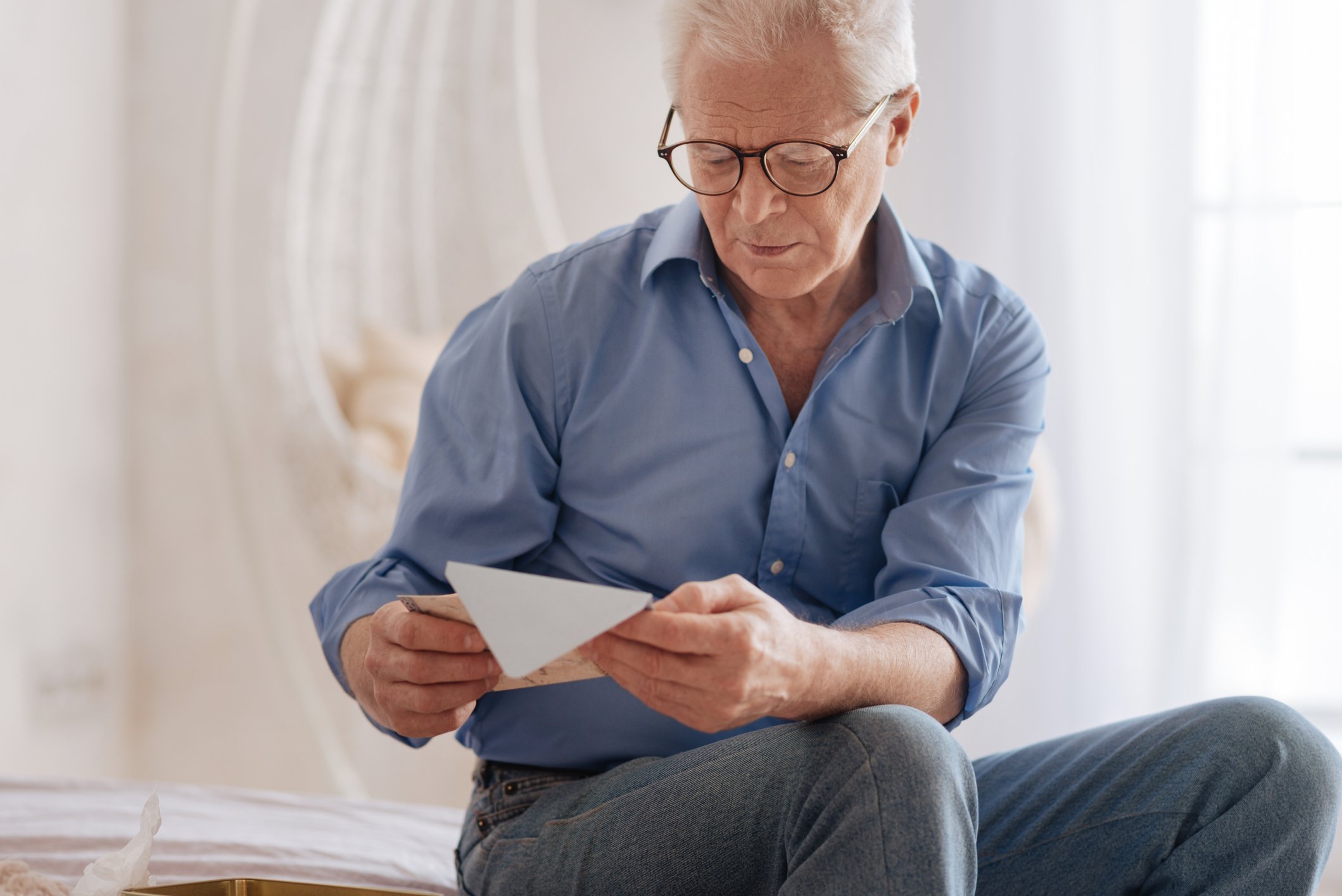 A seated senior man looks down at an envelope in his hands.