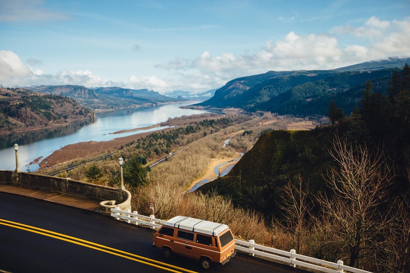 Small conversion van crossing a bridge over a river going between mountains.
