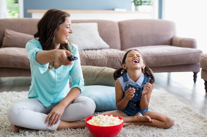 Mother and daughter sharing a bowl of popcorn in front of the TV. Both are smiling and laughing.