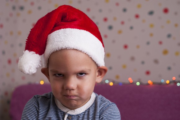 Frowning child wearing Santa elf hat.
