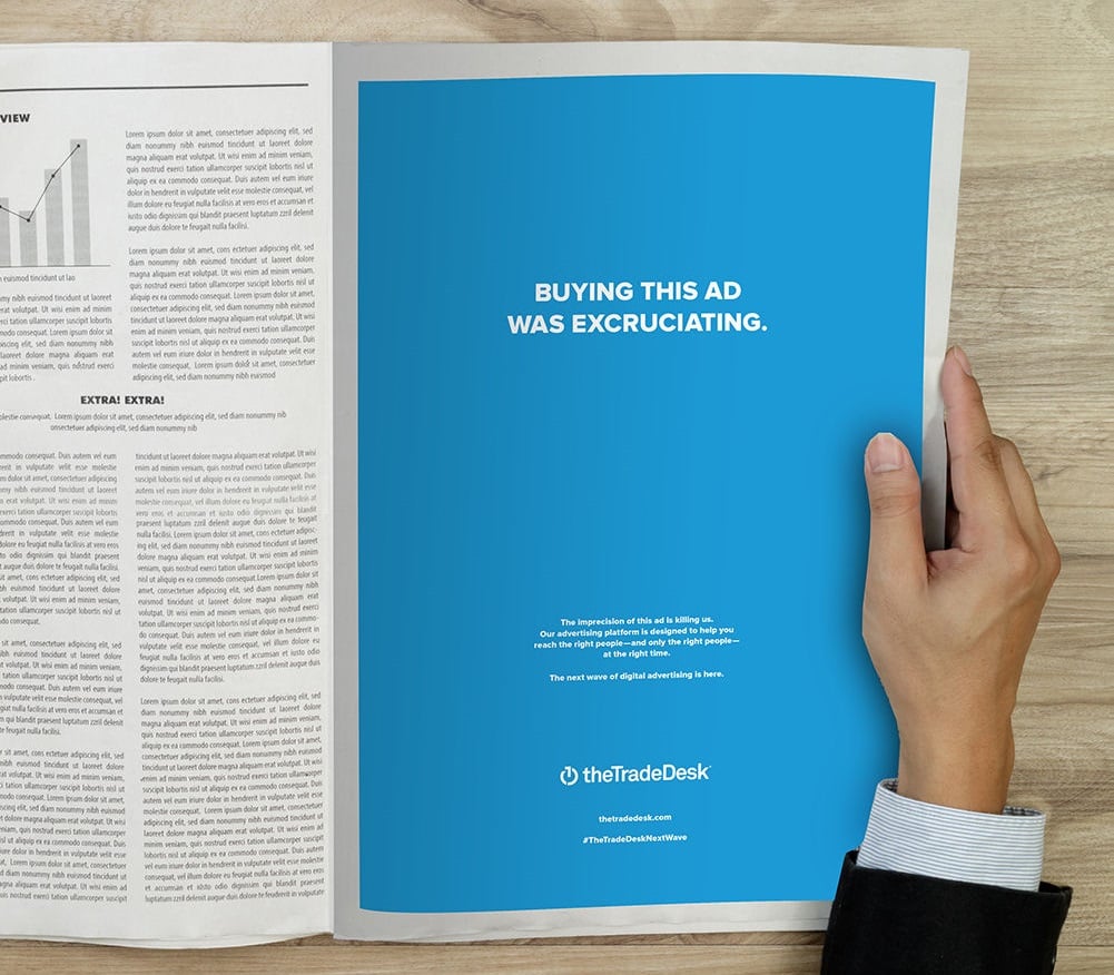 Hand holding paper with Trade Desk ad in blue.