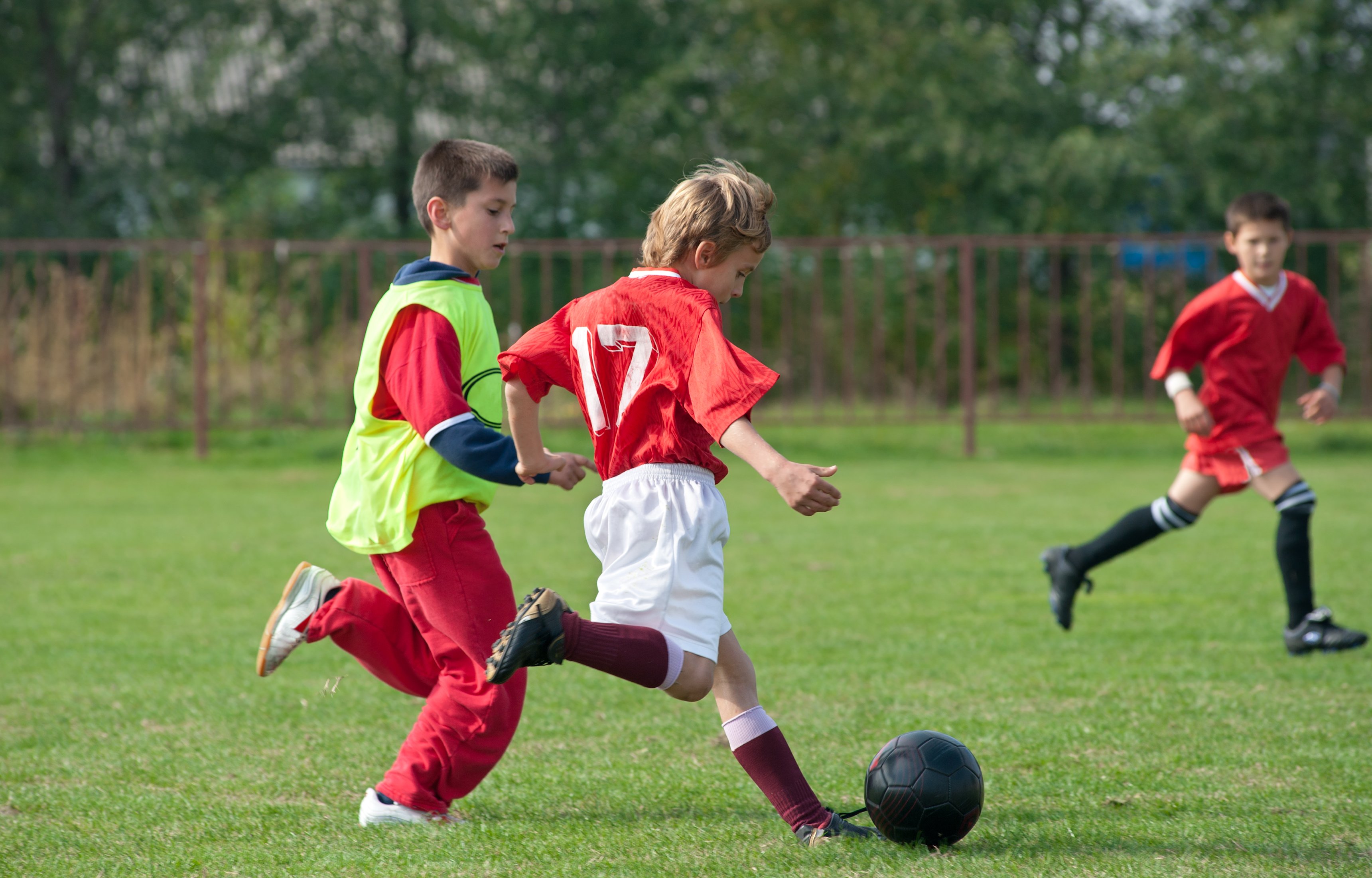 Three boys in uniform playing soccer on a field.