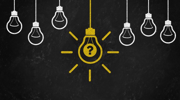 Chalkboard drawing of six small white light bulbs and one larger yellow light bulb with a question mark in the center of it