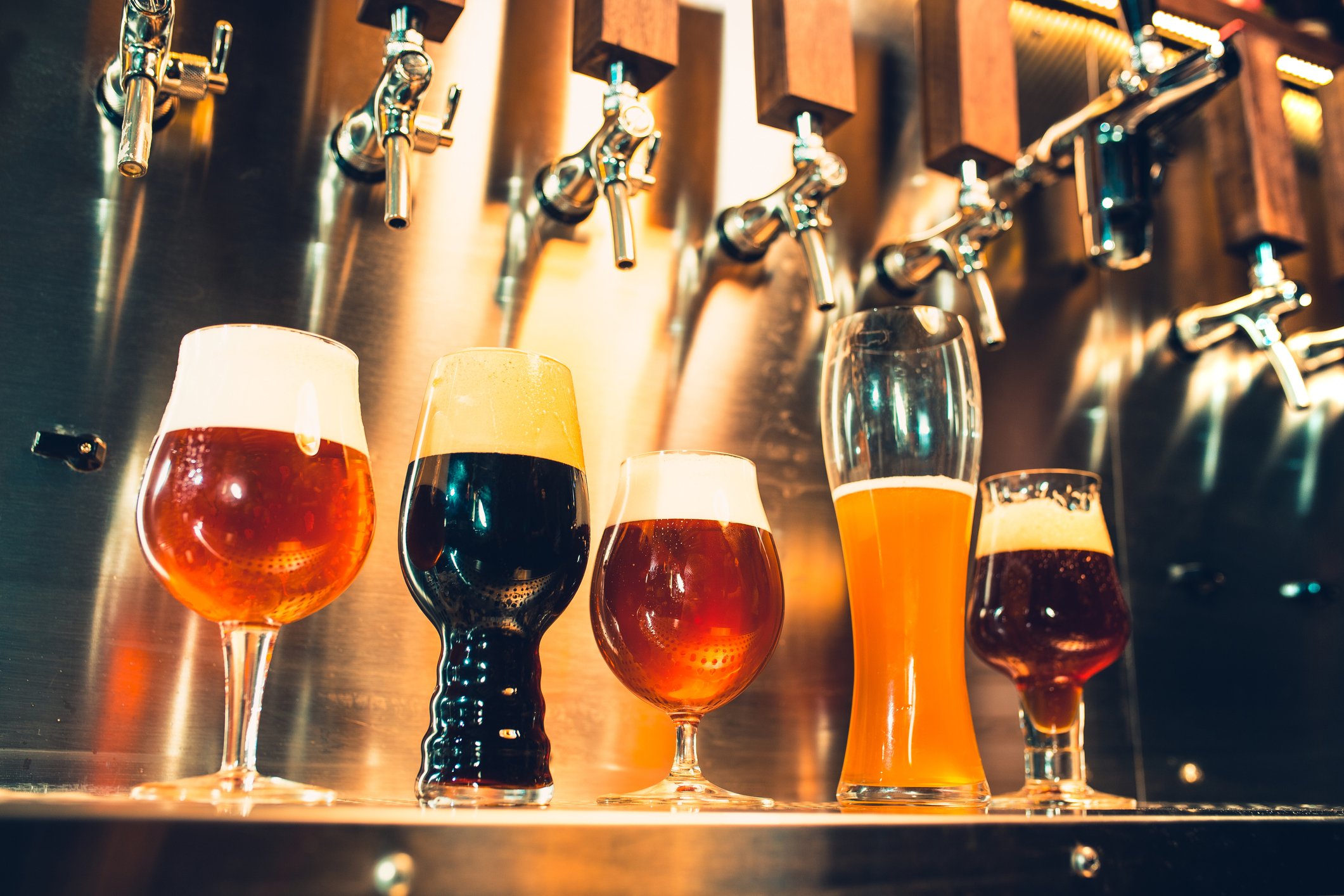 Five tap beers in different type of glasses poured at a bar. 
