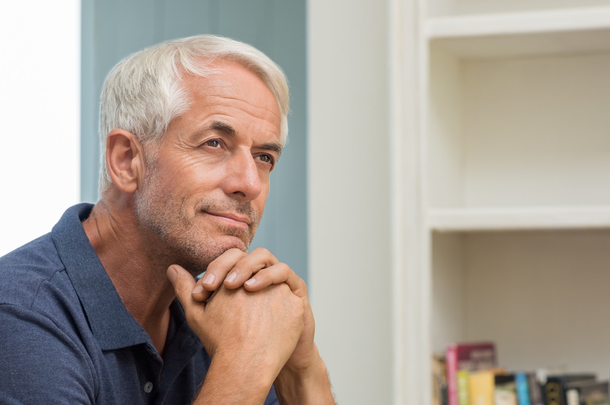 An older man resting his head against his clasped hands, deep in thought