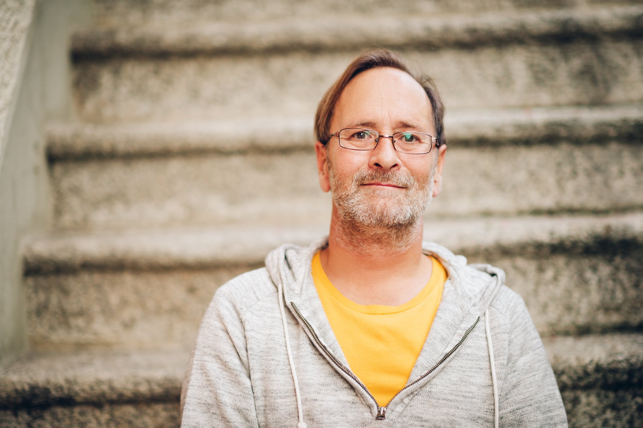 Middle-aged man sitting on stairs wearing gray sweatshirt over yellow t-shirt