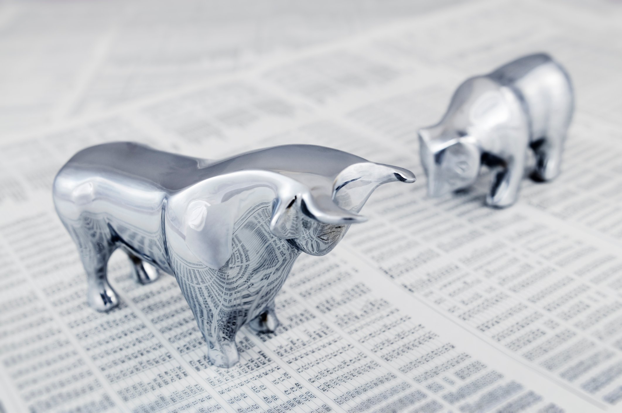 Chrome bull and bear figurines standing on top of a newspaper with stock market data.