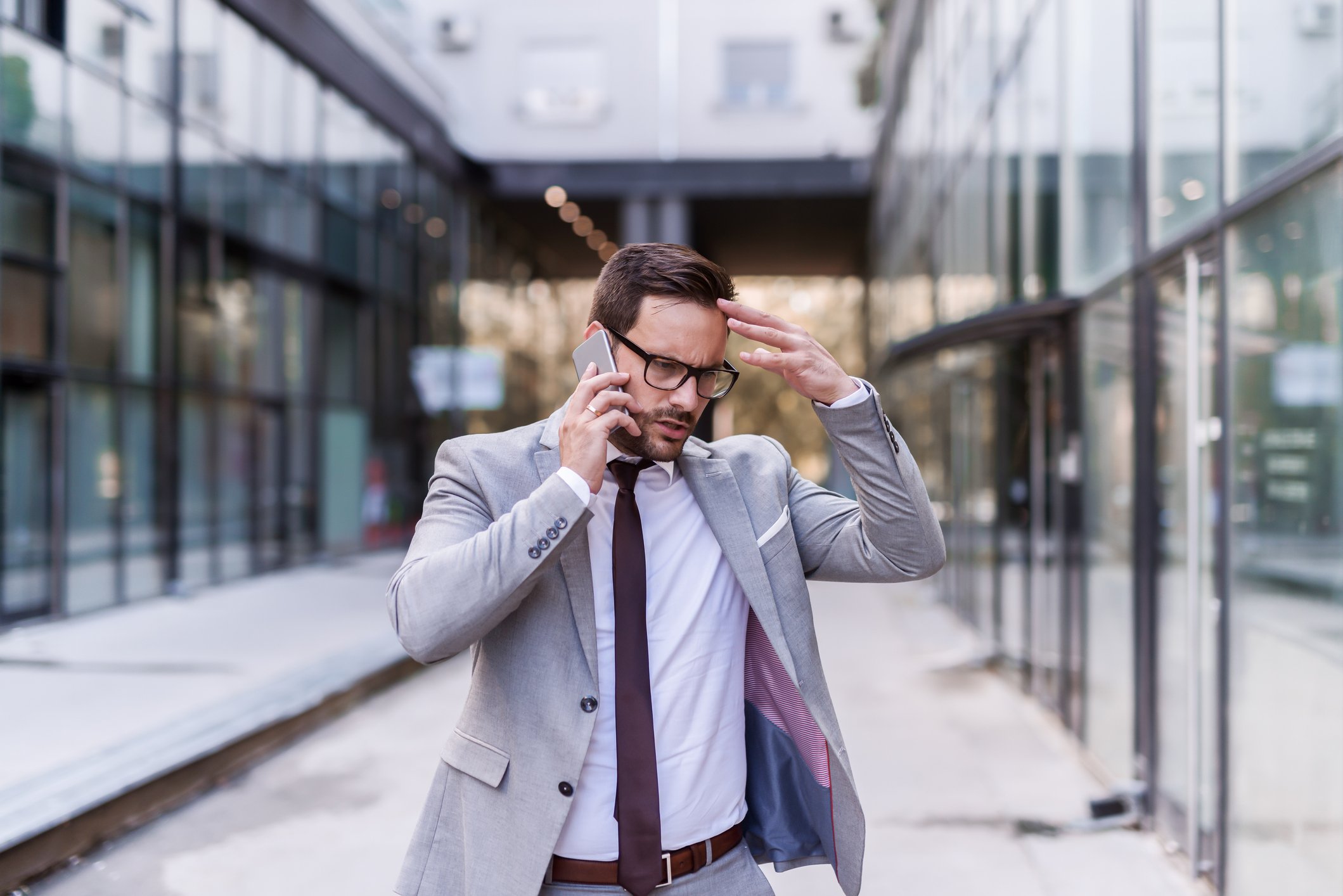 Man in business suit talking on phone outdoors and holding head