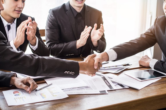 Men in suits shaking hands over a table covered in papers