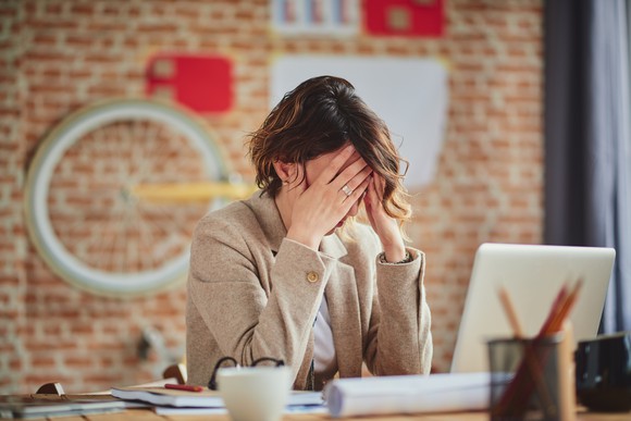 Woman sitting at a laptop, with hands over her face