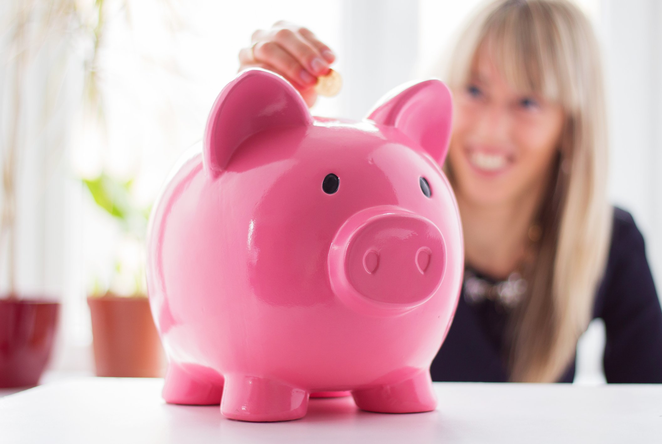 A woman adding a coin to a piggy bank.