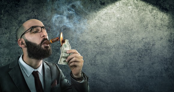 A man smokes a cigar by burning cash.