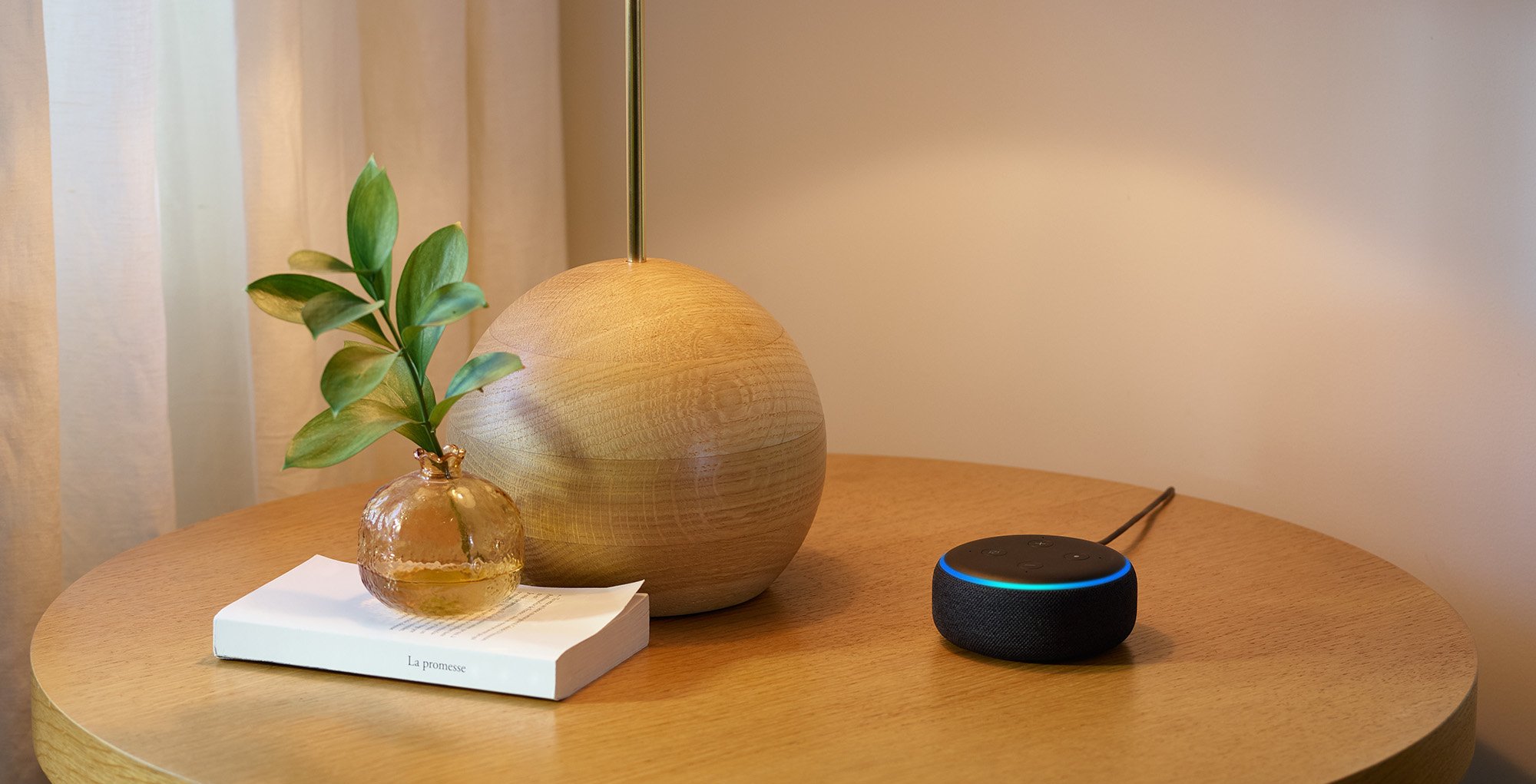 Echo Dot on a side table next to a lamp and a book