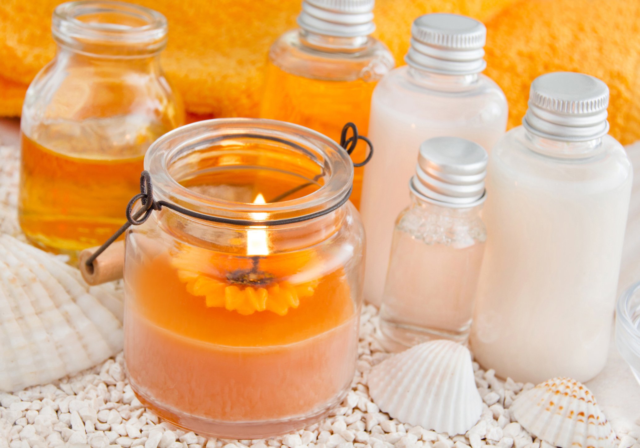 An orange candle sitting next to bottles of white lotion and seashells
