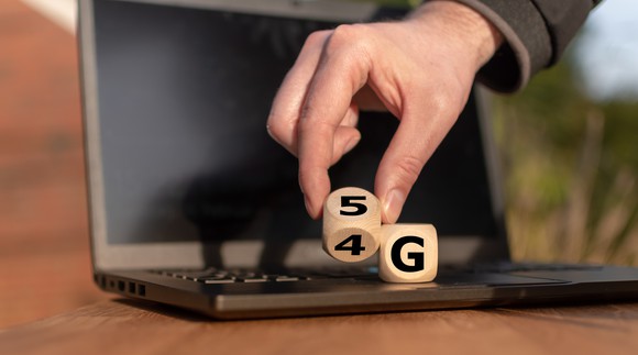 A man turns over blocks spelling out "5G" on a laptop's keyboard.