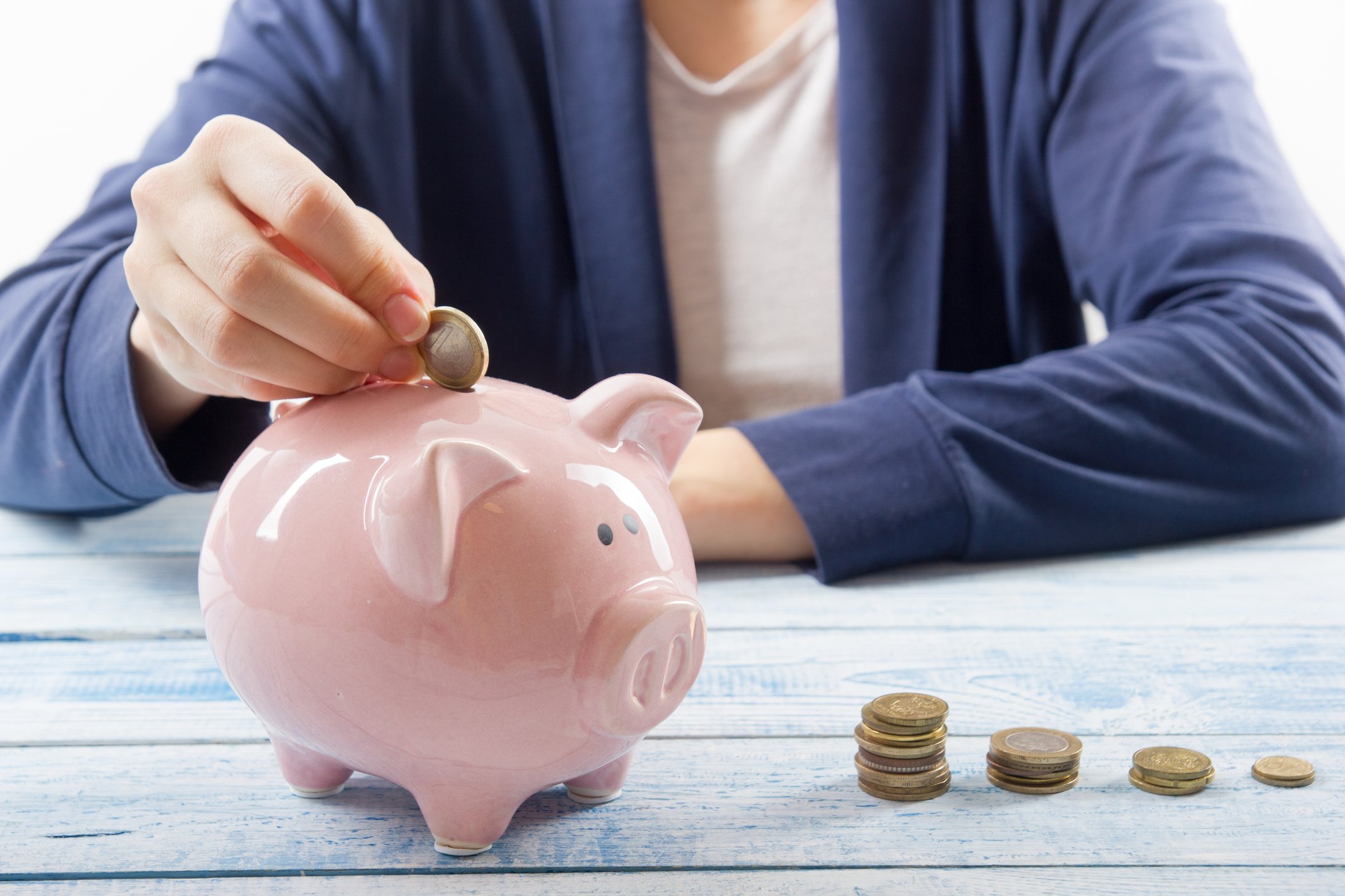 Person putting coins into a piggy bank, with stacks of coins nearby