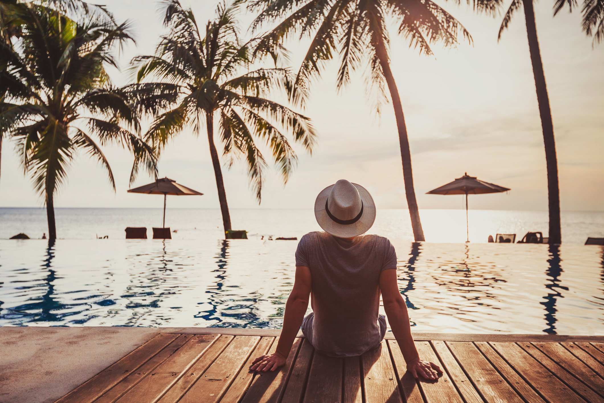 Man in hat sitting by water, staring out at trees