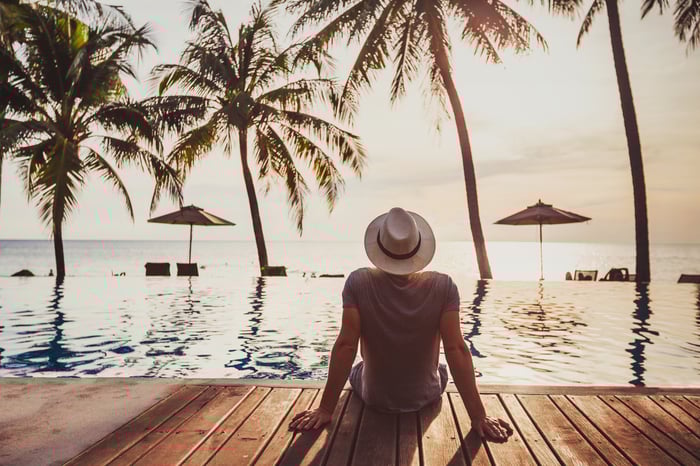 Man in hat sitting by water, staring out at trees