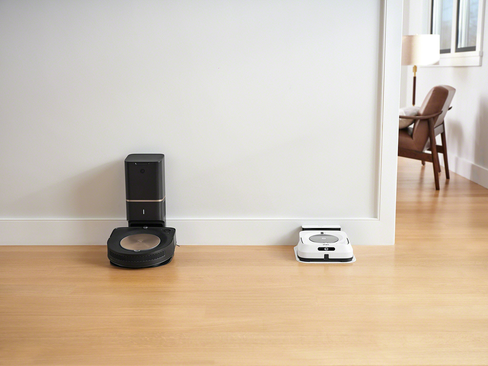 iRobot's new Roomba s9+ and Braava jet m6 docked near each other along a baseboard.