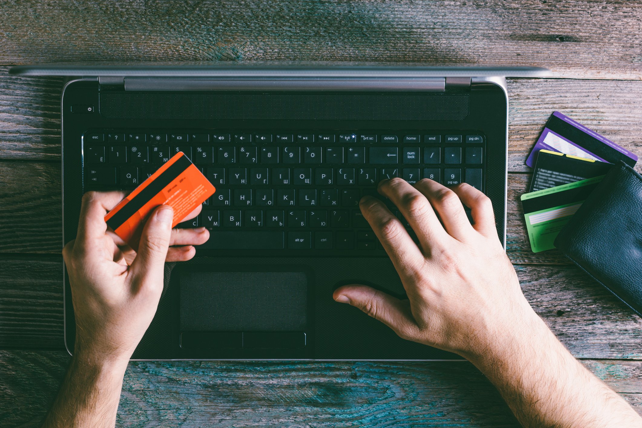 Man holding credit card in left hand while using laptop with his right one.
