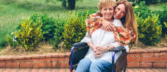 Woman putting arms around older woman sitting in wheelchair