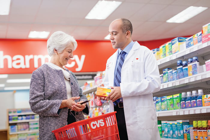 A pharmacist chatting with a senior woman about health products in the pharmacy aisle.