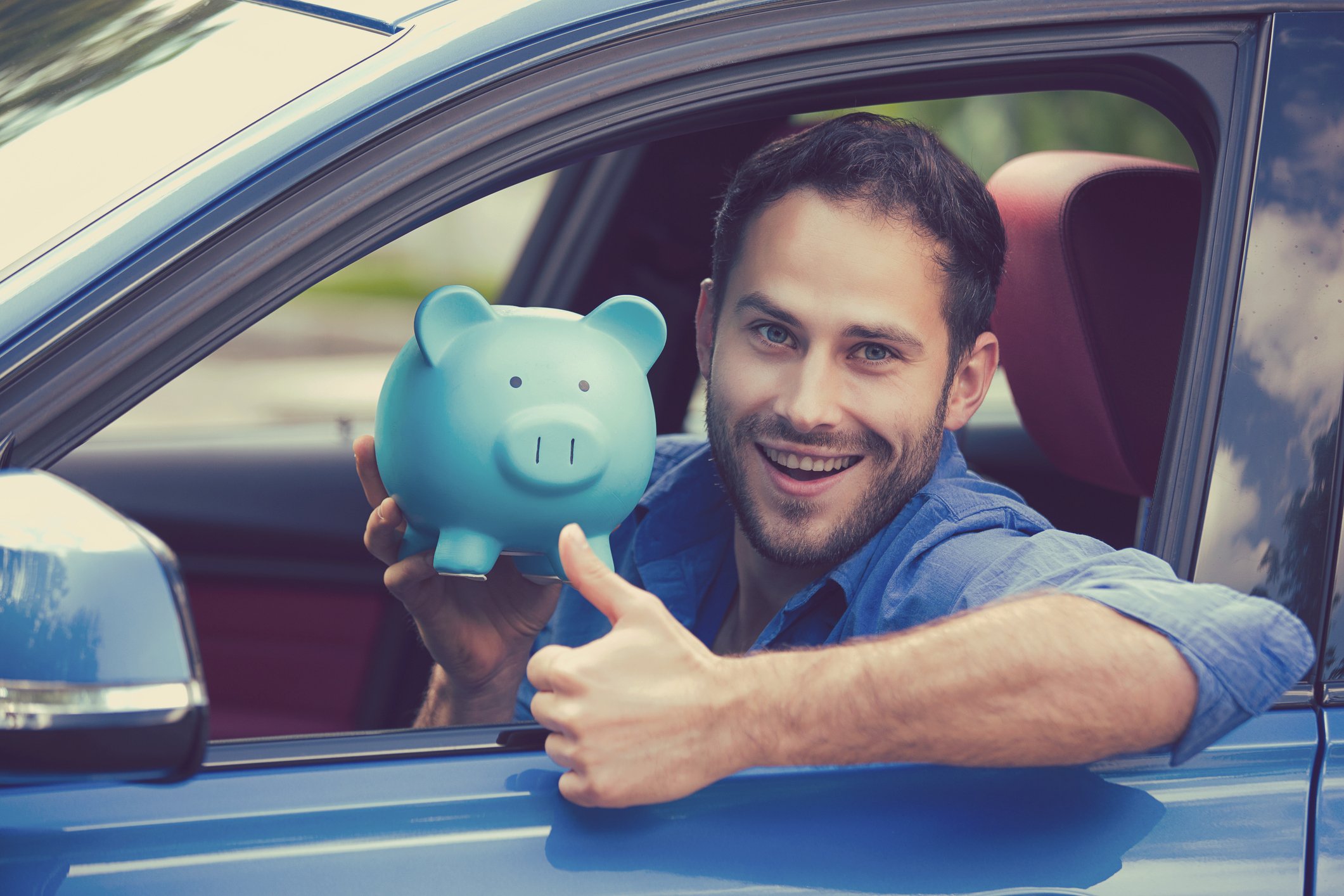 Man in a car holding a piggy bank, while giving a thumbs-up sign