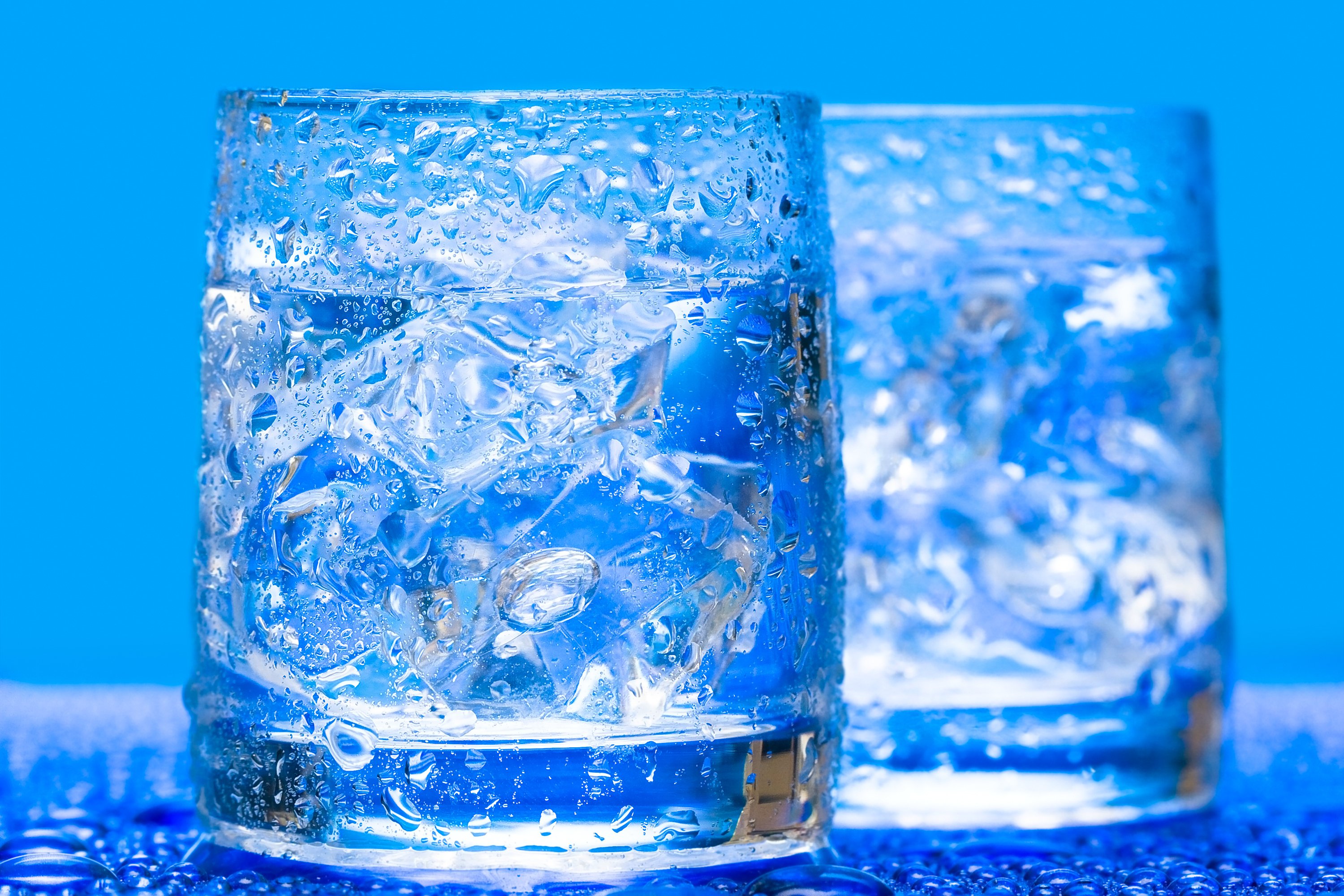 Tw glasses of ice water with blue background.