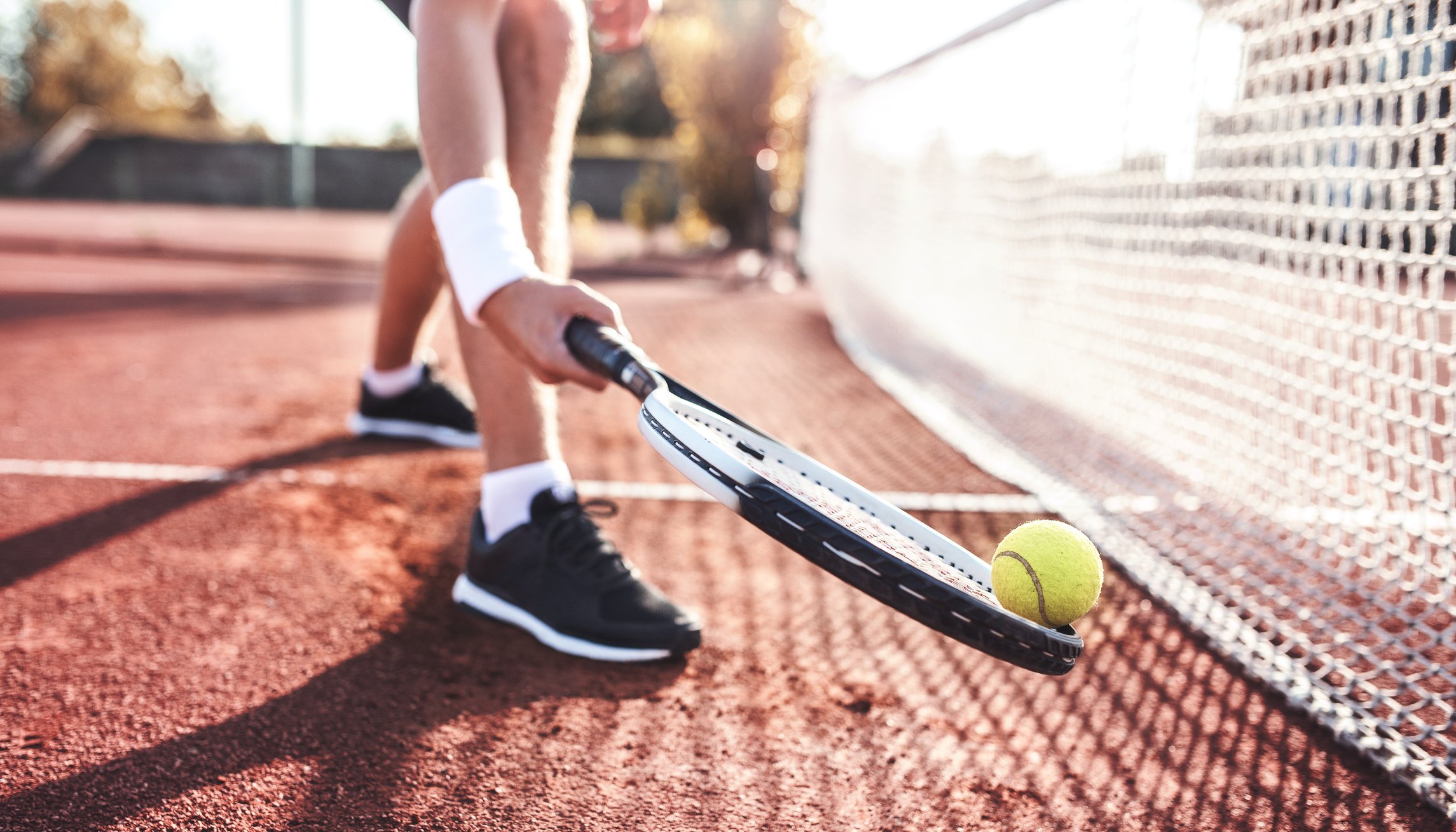 A tennis player stands near the net on a clay court.