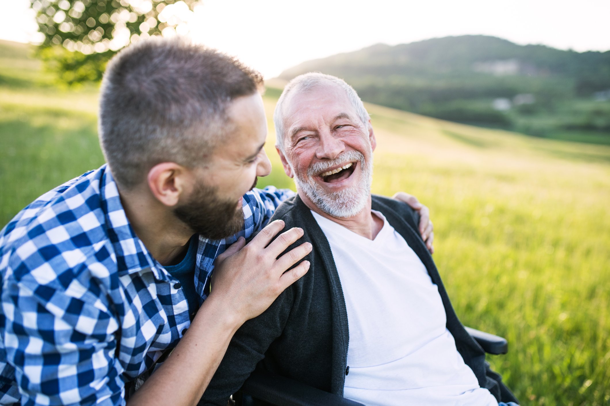 Young man putting arms around smiling older man out in a field