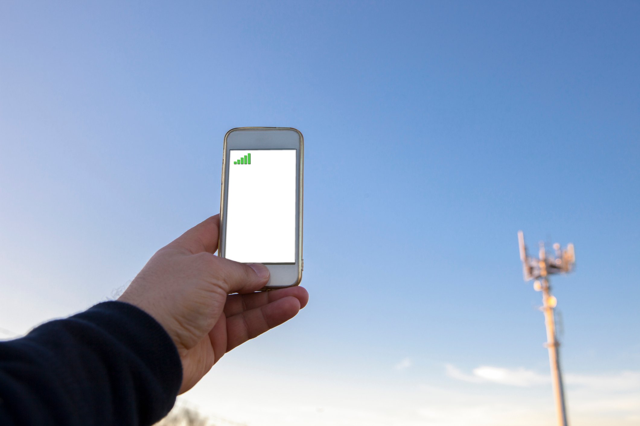 A man holds a smartphone up near a cellular tower.