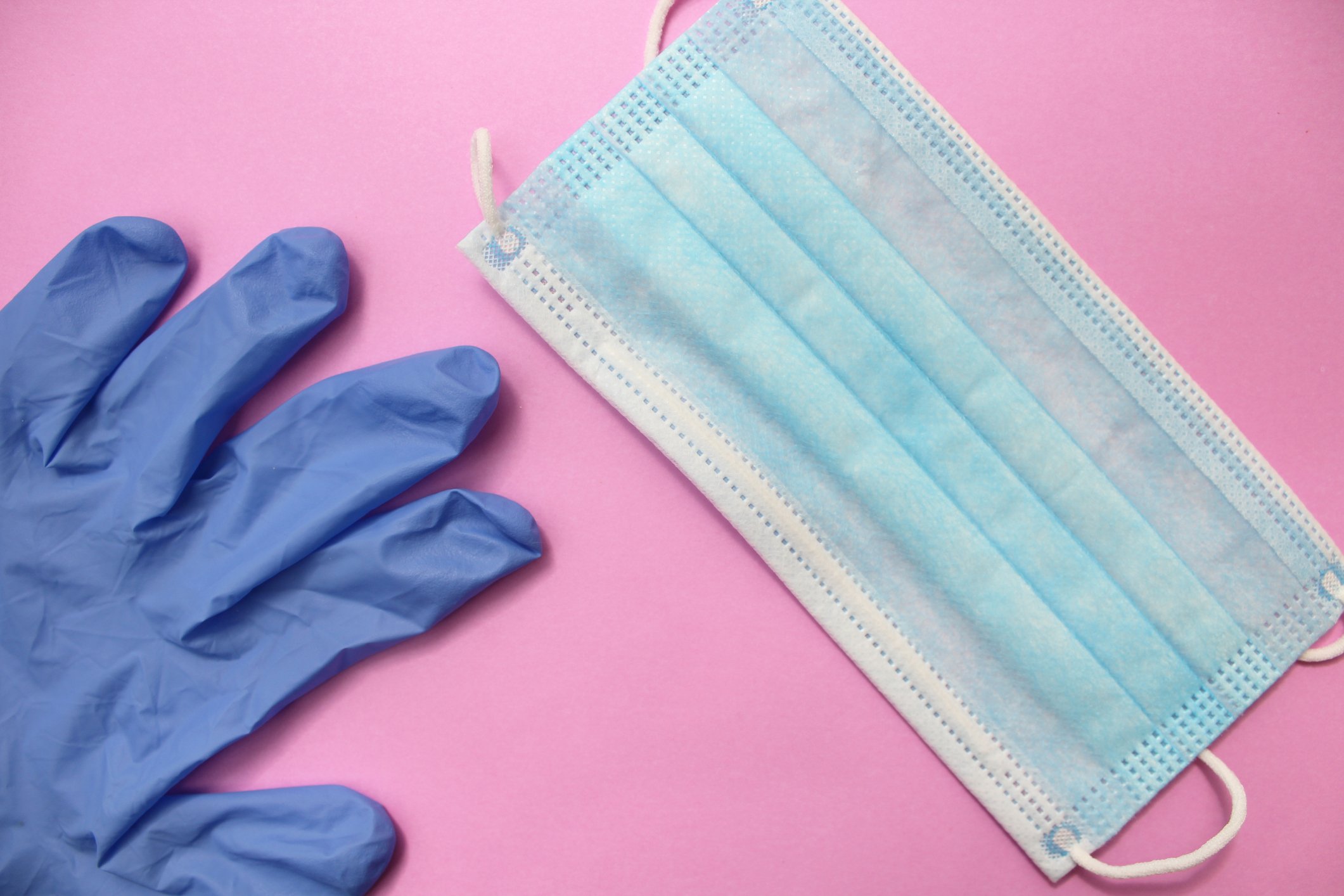 Blue disposable gloves and face mask on a pink surface.