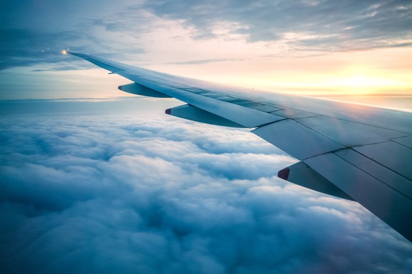 An airplane wing above the clouds with the sun setting behind the clouds on the horizon.