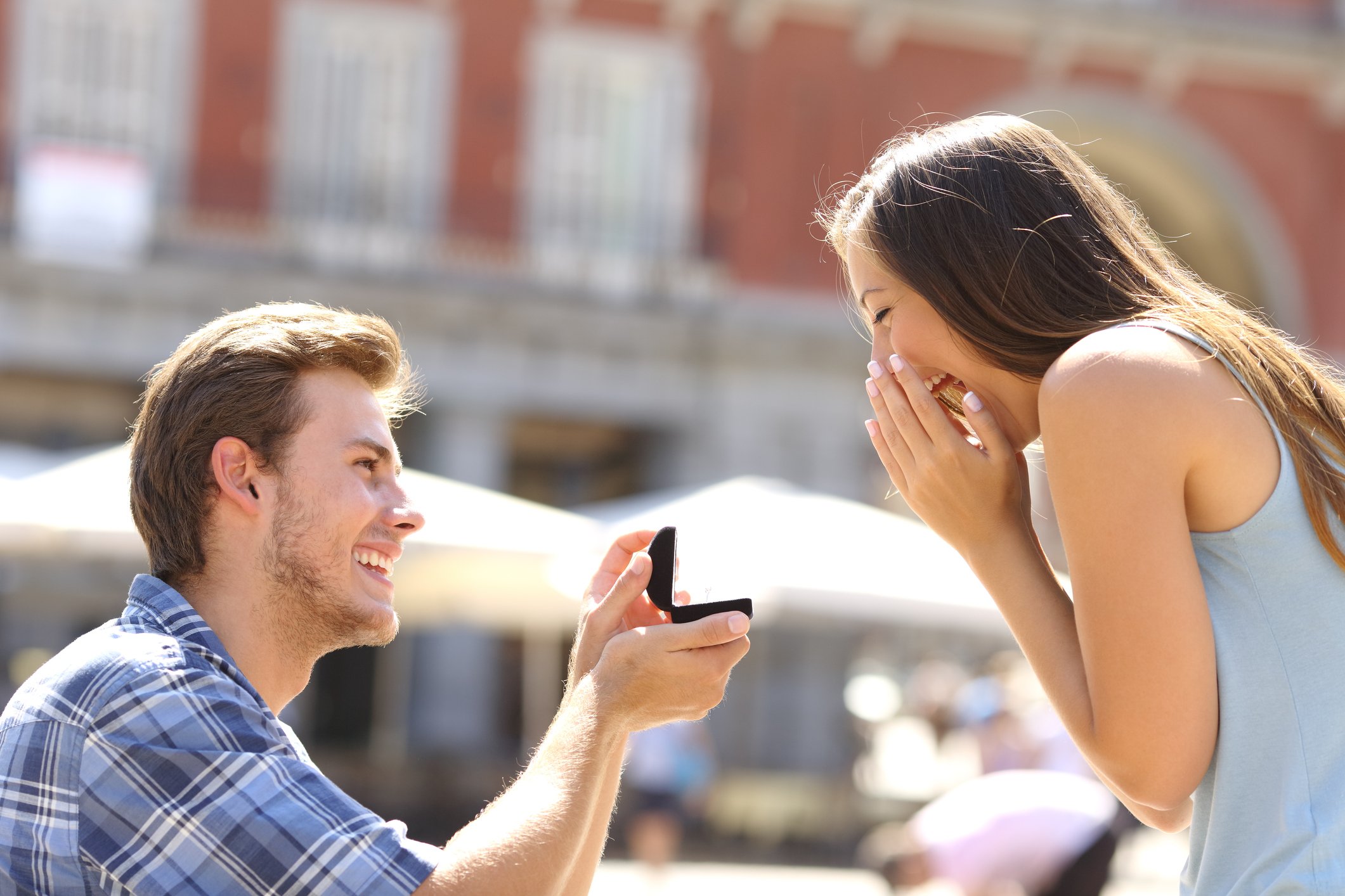 Man holding up open jewelry box while smiling woman covers her face