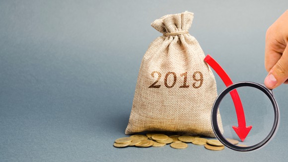 Bag with 2019 printed on it, gold coins beside it, and a red arrow pointing down extending from it with a hand holding a magnifying glass over the red arrow