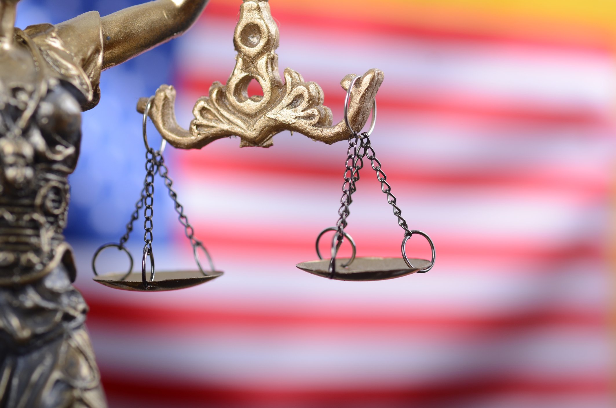 Statue of Lady Justice with two empty scales dangling in front of an American flag. 