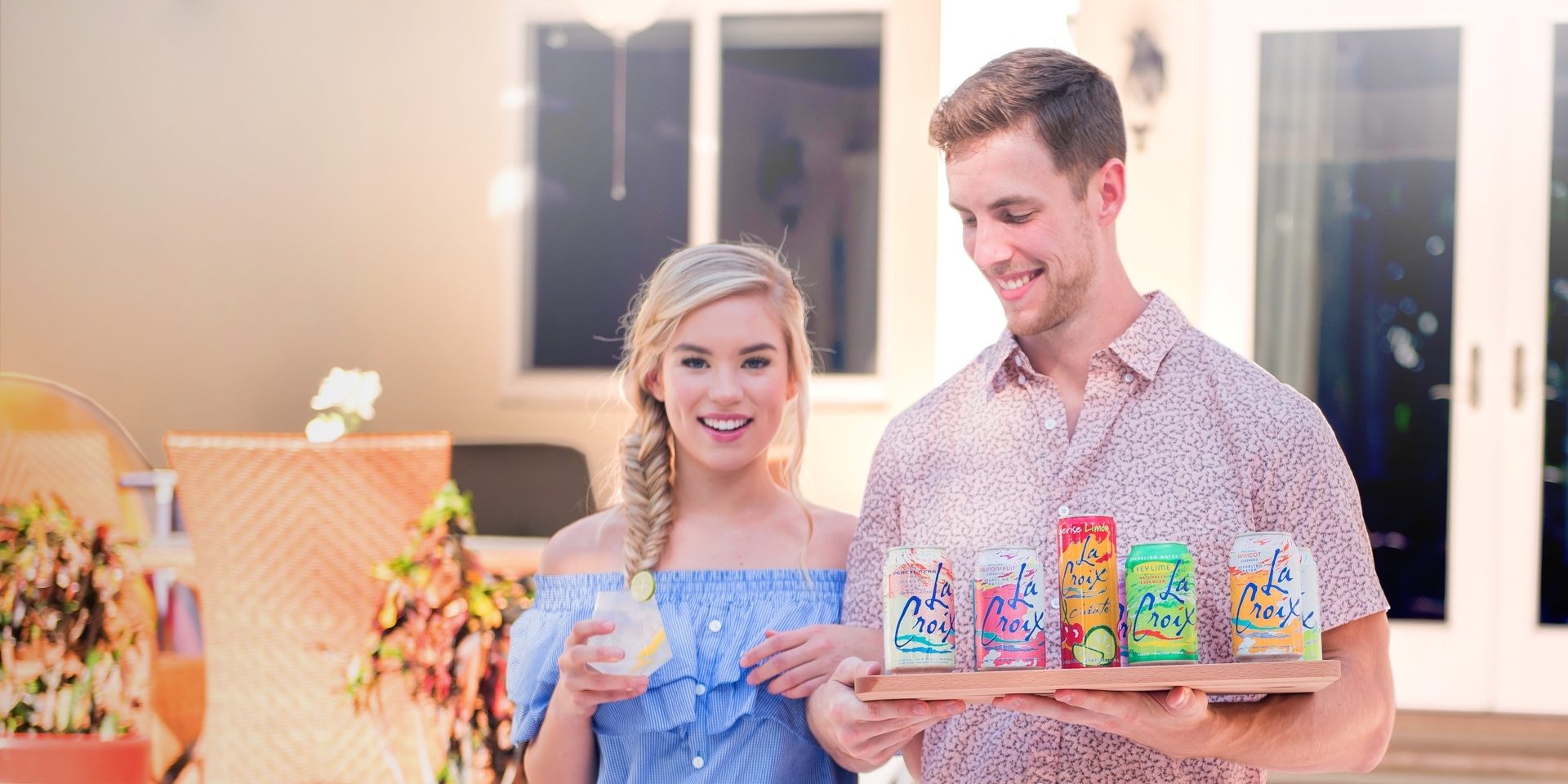 A man holding multiple cans of LaCroix, standing next to a woman holding a glass with clear liquid.