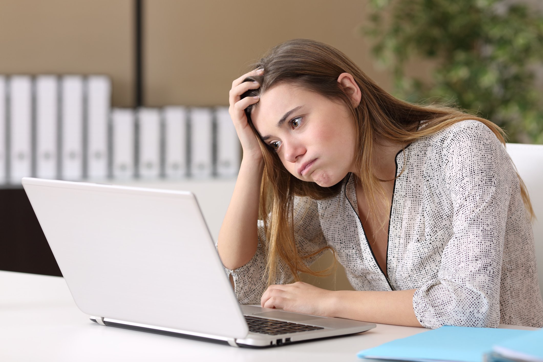 Young woman at laptop resting her head on her hand with bored expression
