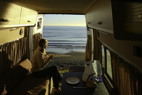 A young woman eats breakfast in an RV parked by the sea.